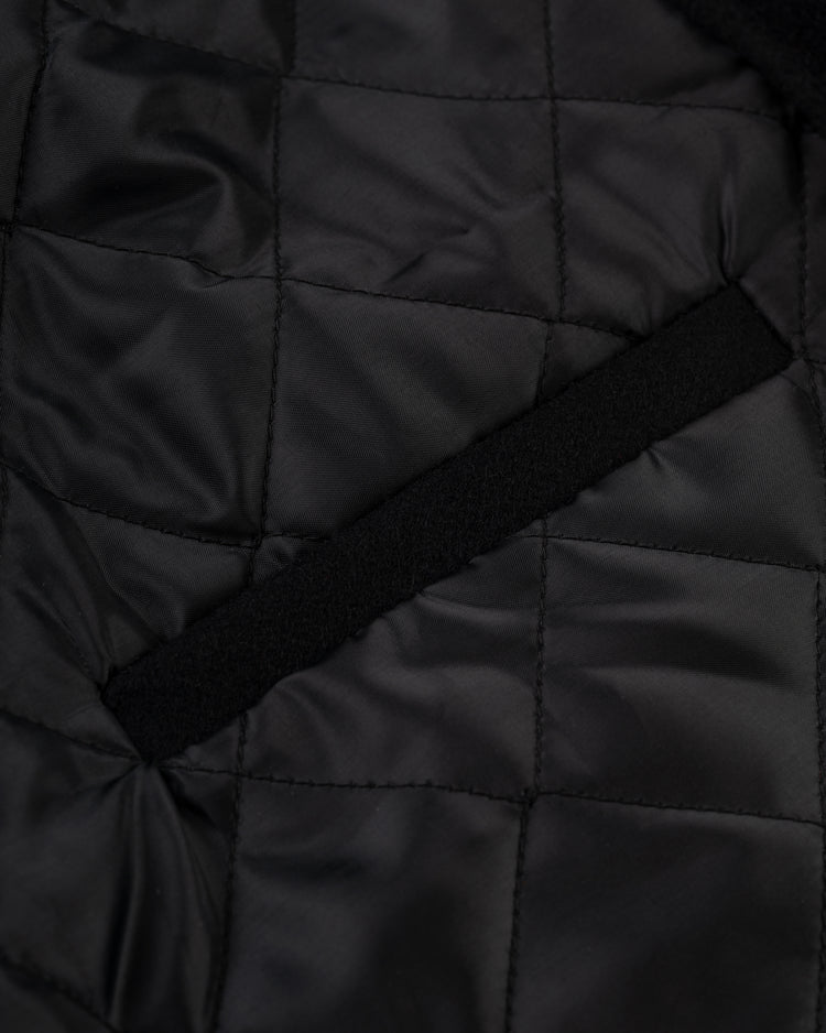 Close-up of black quilted fabric with square stitching and a diagonal slit pocket, highlighting the classic details of the Ebbets Field Negro League Wool & Leather Varsity Jacket.