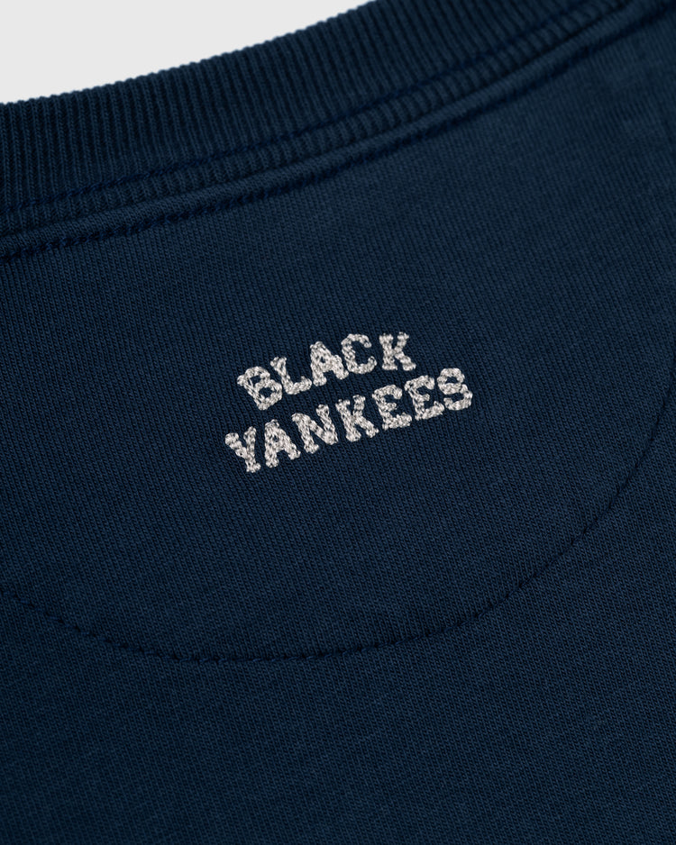 Close-up of an Ebbets Field New York Black Yankees Embroidered NY Long Sleeve Pocket Tee in navy, featuring BLACK YANKEES stitched in white thread below the back collar.