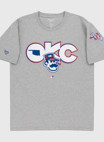 The Ebbets Field Oklahoma City 89Ers MiLB Fashion Cotton Short Sleeve Tee is a heather gray T-shirt with a large logo and cartoon character on the chest, plus 405 patches and other symbols on the sleeves.