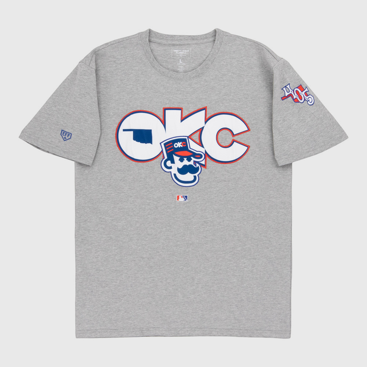 The Ebbets Field Oklahoma City 89Ers MiLB Fashion Cotton Short Sleeve Tee is a heather gray T-shirt with a large logo and cartoon character on the chest, plus 405 patches and other symbols on the sleeves.