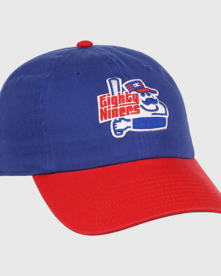 The Ebbets Field Oklahoma City 89Ers MiLB Logo Dad Ballcap is blue with a red brim, featuring an embroidered cartoon character holding a bat and “Eighty Niners” text on the front.