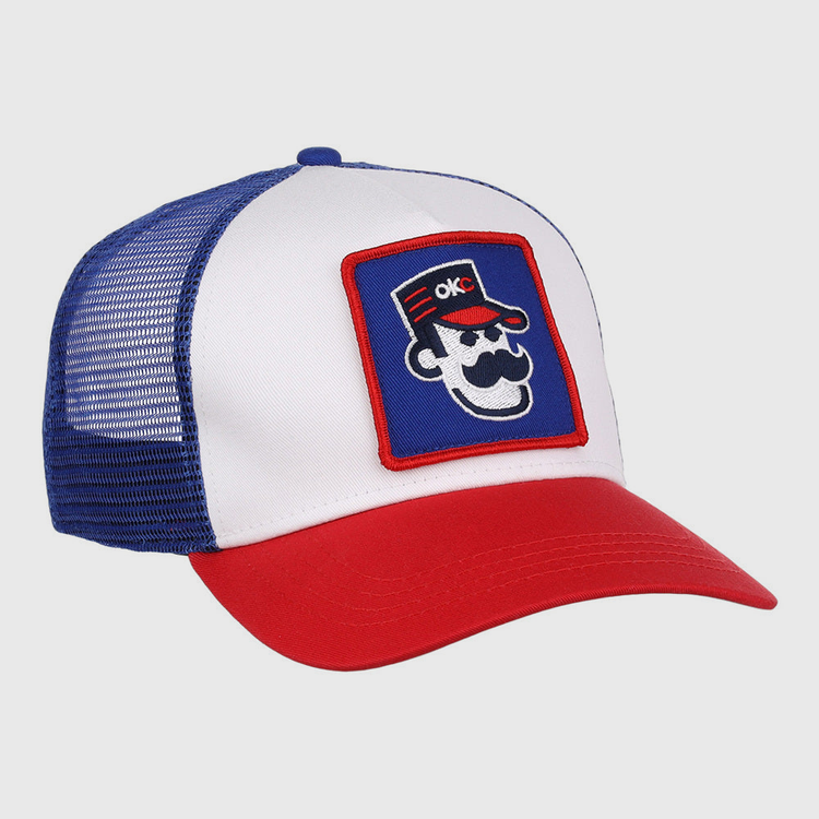 The Ebbets Field Oklahoma City 89Ers MiLB Trucker Ballcap features a white front panel, blue mesh back, red brim, and a patch of a cartoon face with sunglasses, mustache, red hat, and OKC letters.