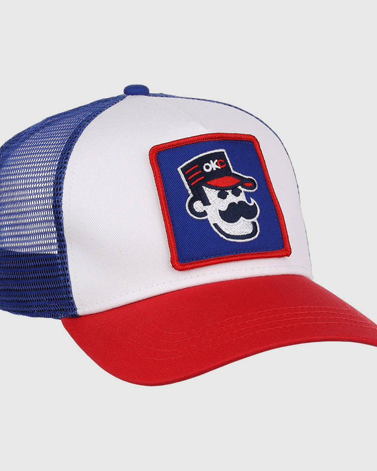 The Ebbets Field Oklahoma City 89Ers MiLB Trucker Ballcap features a white front panel, blue mesh back, red brim, and a patch of a cartoon face with sunglasses, mustache, red hat, and OKC letters.