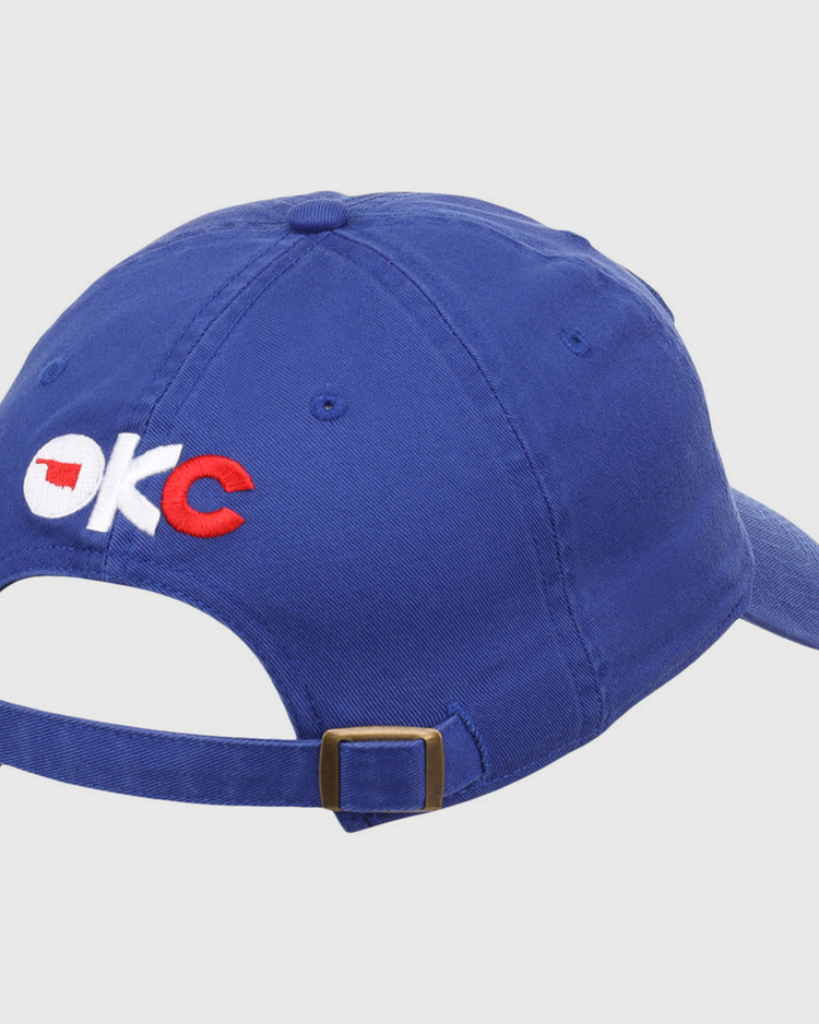 The Ebbets Field Oklahoma City Dodgers MiLB Dad Ballcap is blue, features OKC embroidered on the back in white and red with an Oklahoma outline in the O, and has an adjustable brass-buckle strap.