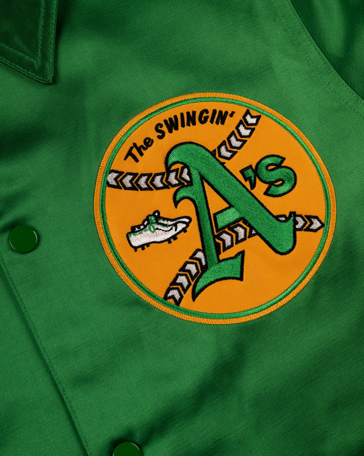 The EFF Oakland Athletics 1971 Authentic Satin Windbreaker Jacket features a large yellow patch with “The Swingin As,” a green A, baseball cleats, and an illustrated shoe—ideal for MLB vintage windbreaker fans.