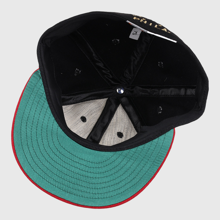 The EFF Philadelphia Stars Gilded Collection Ballcap is flipped upside down to reveal its green underside brim with red trim, black interior panels, blue center button, and a visible size tag—ideal for any Negro National League collector.