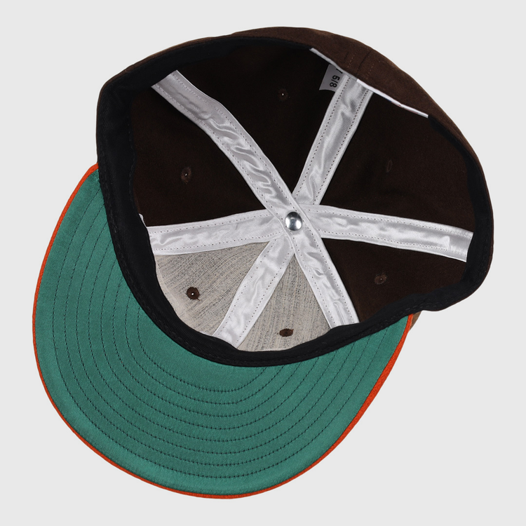 The image shows the inside of an EFF Pine Bluff Judges 1953 Vintage Ballcap, featuring a green brim with orange edge, brown panels, white cross-shaped stitching, and a silver button.