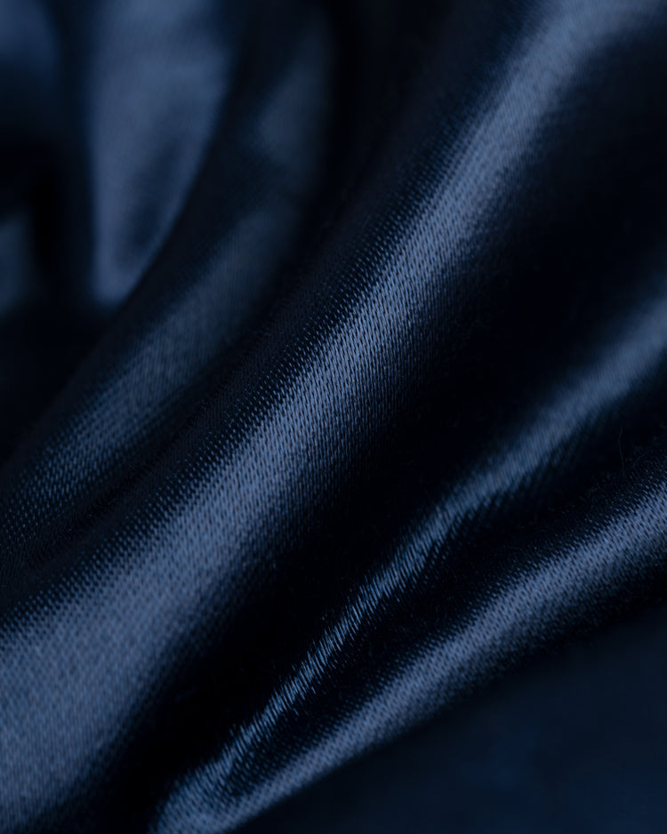Close-up of the dark blue, shiny satin fabric of the EFF Philadelphia Phillies 1937 Authentic All Satin Varsity Jacket, featuring smooth folds and a soft, reflective texture that catches light for dynamic shades of blue.