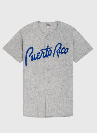 The Ebbets Field Puerto Rico 1958 National Team Authentic Wool Road Baseball Jersey is gray with short sleeves, blue Puerto Rico script on the chest, a button-up front, and a small neck tag.