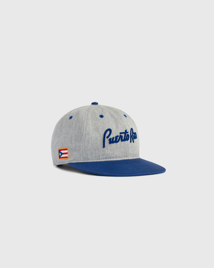 The Ebbets Field Puerto Rico 1958 National Team Cotton Twill Ballcap features a gray crown, blue brim and button, Puerto Rico embroidered in blue script, and a Puerto Rican flag patch—perfect for fans of Roberto Clemente.