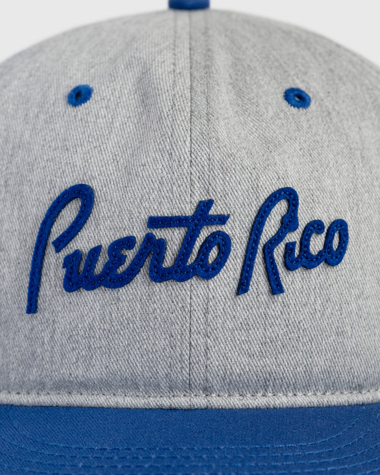 The Ebbets Field Puerto Rico 1958 National Team Cotton Twill Ballcap features gray cotton twill, blue Puerto Rico cursive stitching on the front, blue eyelets, and a blue bill—ideal for fans of Roberto Clemente and the 1958 Caribbean Series.