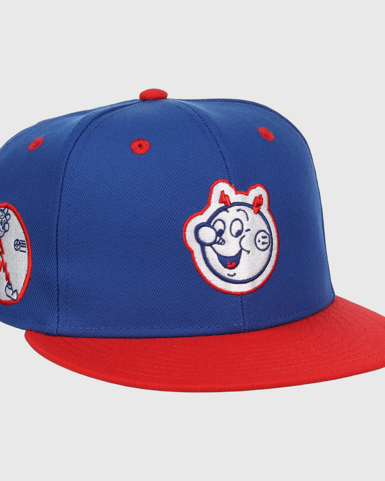 The EFF Reddy Kilowatt EFF DNA Fitted Ballcap features a blue vintage design with a red brim, cartoon bear face front, and side patch of a bear playing baseball—classic style inspired by Ebbets Field Flannels.
