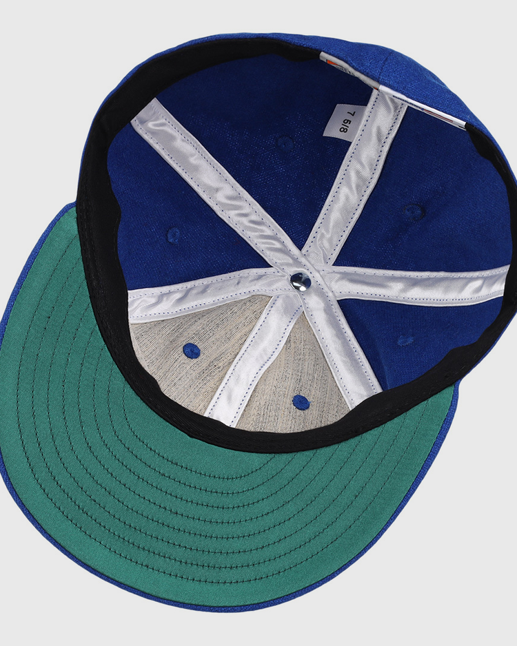 The image shows the inside view of an EFF Royal Ponciana Giants 1912 Vintage Ballcap in blue wool with a green brim, size tag 7 1/8, white and black lining, exposed stitching, and classic hotel league baseball styling.