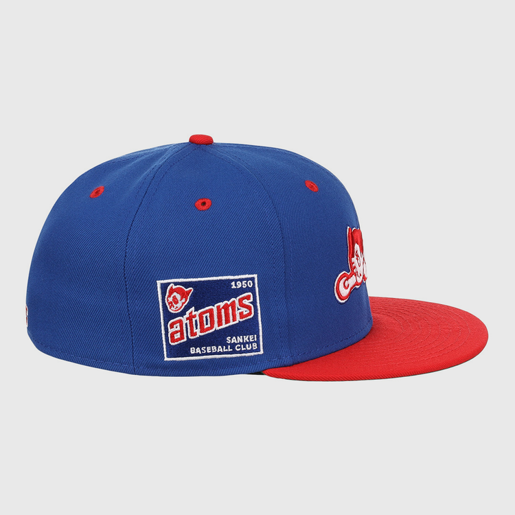 The Sankei Atoms EFF DNA Fitted Ballcap by EFF is a blue vintage-style cap with a red brim, embroidered patches, and a side patch that reads Atoms 1950 SANKEI BASEBALL CLUB with an Atom Boy mascot.
