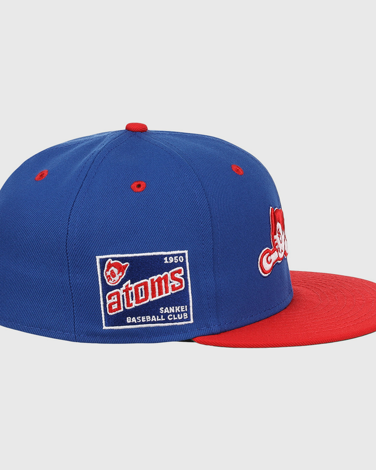 The Sankei Atoms EFF DNA Fitted Ballcap by EFF is a blue vintage-style cap with a red brim, embroidered patches, and a side patch that reads Atoms 1950 SANKEI BASEBALL CLUB with an Atom Boy mascot.