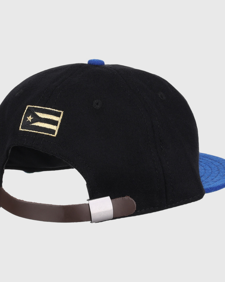 The EFF Santurce Cangrejeros Gilded Collection Ballcap is black with a blue brim, seen from the back. It has an adjustable brown strap and a small gold and white flag detail on the left side, inspired by Puerto Rico League heritage.
