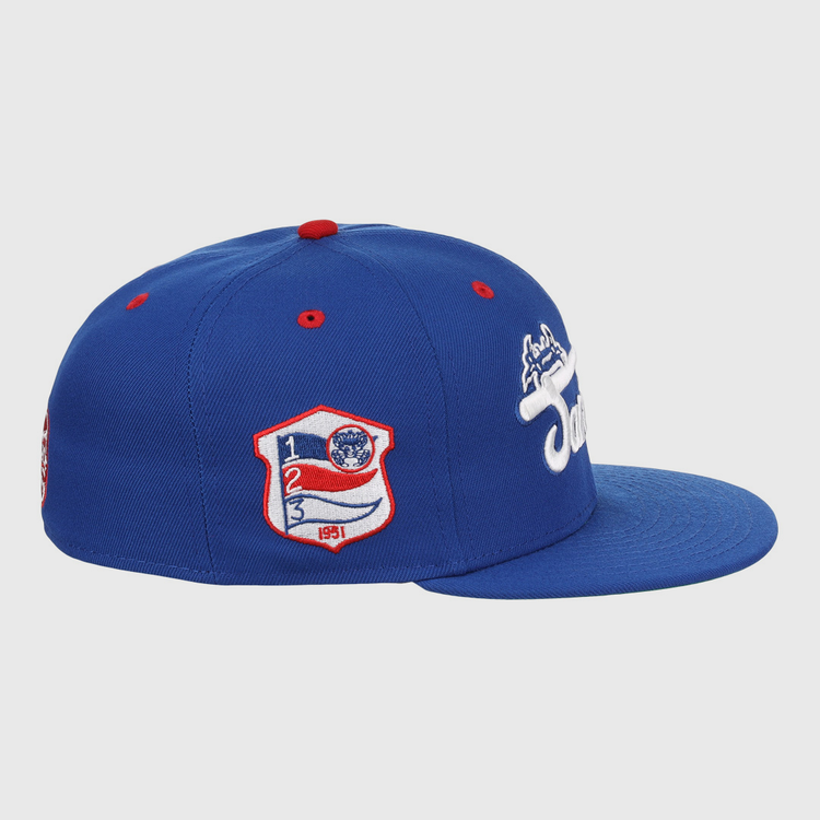 The EFF Santurce Cangrejeros NLB Team Color Fitted Ballcap is a blue vintage-style cap with a flat brim, side white embroidered logo, and a red, white & blue Puerto Rican League patch featuring numbers and shield on the front side panel.