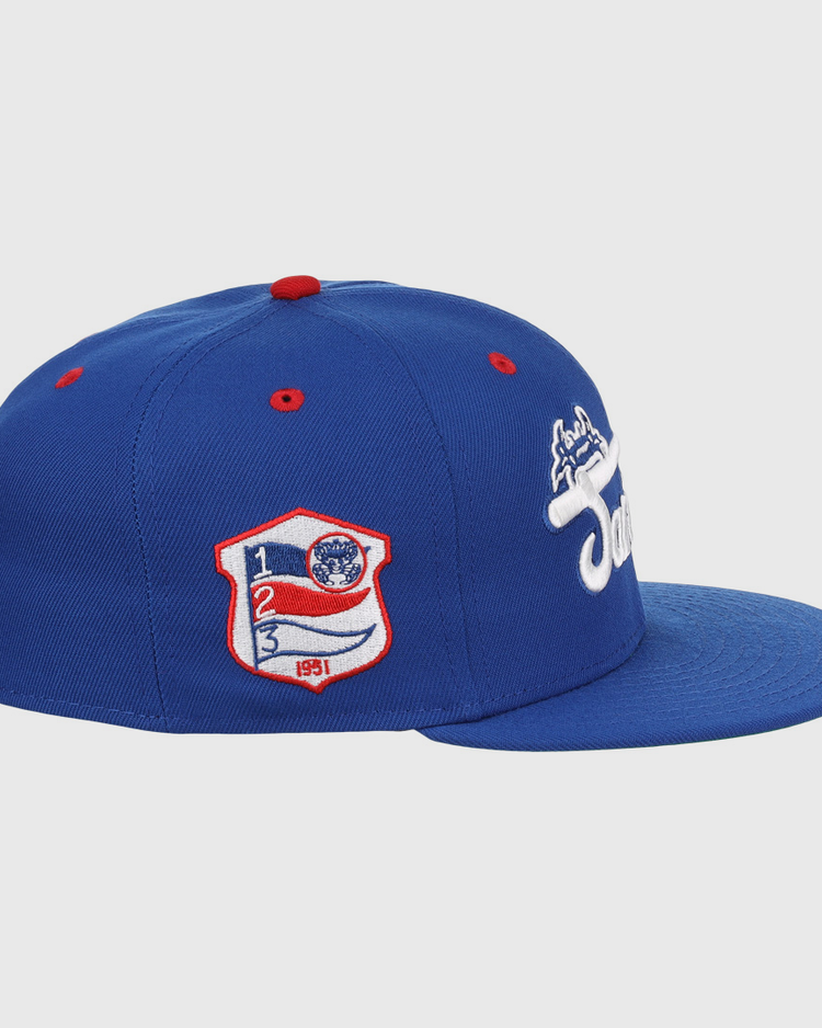 The EFF Santurce Cangrejeros NLB Team Color Fitted Ballcap is a blue vintage-style cap with a flat brim, side white embroidered logo, and a red, white & blue Puerto Rican League patch featuring numbers and shield on the front side panel.