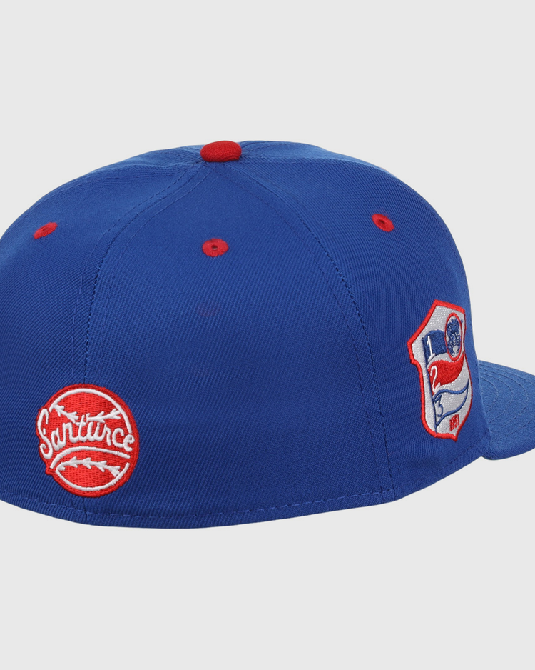 The EFF Santurce Cangrejeros NLB Team Color Fitted Ballcap is a vintage-inspired blue cap with red accents, featuring two embroidered patches: a round red Santurce logo and a shield patch with a flag and number 21 from the Puerto Rican League.