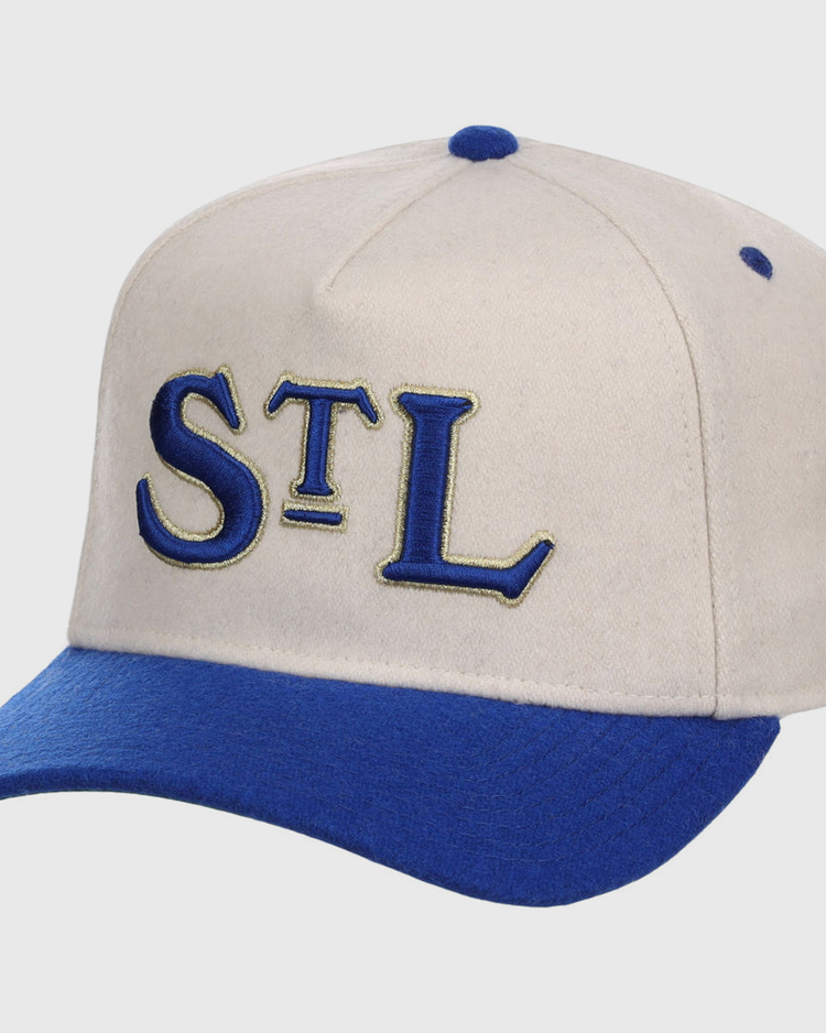 The Ebbets Field St. Louis Stars NLB Ballpark A-Frame Ballcap is beige with a royal blue brim and top button, featuring “STL” embroidered in blue and gold on the front.