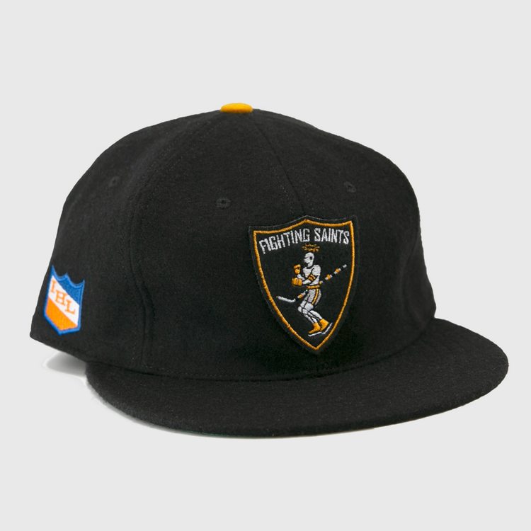 The EFF St. Paul Fighting Saints 1961 Vintage Ballcap is a black cap featuring a skeleton-hockey-stick Fighting Saints logo on the front and a blue/orange shield patch on the side—ideal for any Saints hockey fan.