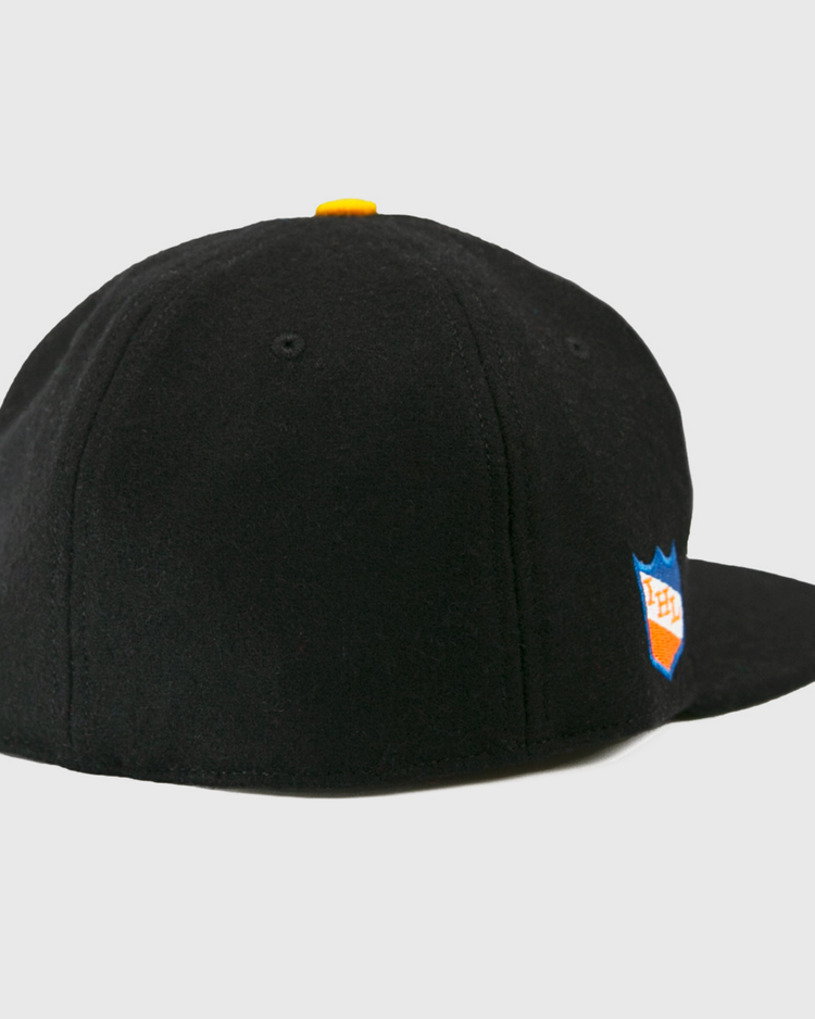 The EFF St. Paul Fighting Saints 1961 Vintage Ballcap is a black wool cap with a yellow top button, blue and orange shield logo on the right side, and classic styling inspired by the Saints hockey team.