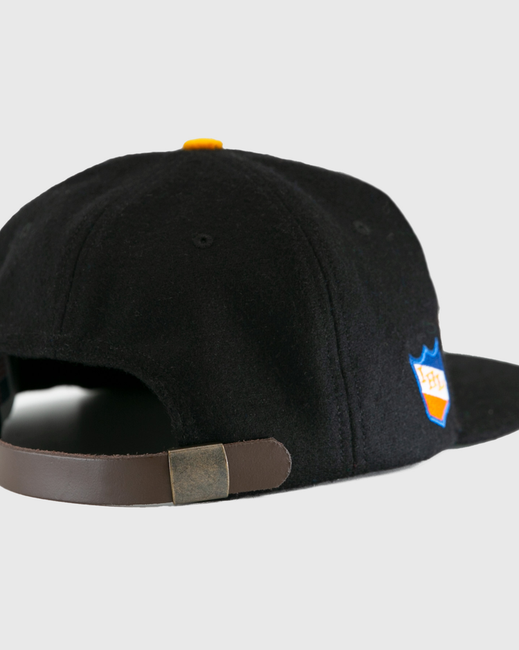 The EFF St. Paul Fighting Saints 1961 Vintage Ballcap in black features a brown adjustable strap with metallic clasp, a side patch, and classic wool cap style—a tribute to vintage Saints hockey team caps.