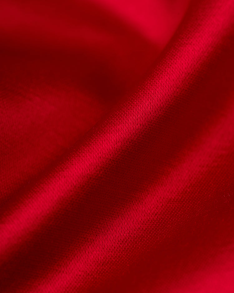 A close-up of smooth, red satin fabric with gentle folds and a shiny finish evokes the soft texture and rich hue of the EFF Philadelphia Phillies 1950 Satin Windbreaker Jacket.