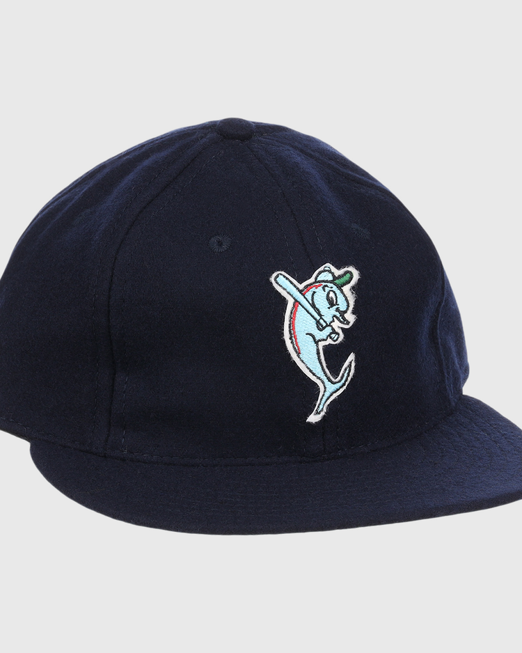 The EFF Tampa Tarpons Letterhead Wool Vintage Ballcap is a navy blue cap with a cartoon dolphin mascot in a green cap and red bat, inspired by Minor League baseball and the playful spirit of the Tampa Tarpons.