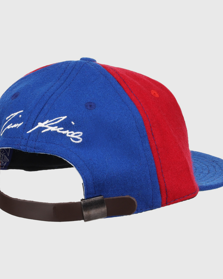 The Ebbets Field Flannels Tim Raines Signature Series Ballcap in blue and red wool features a leather strap with metal clasp and white cursive embroidery above the back opening, capturing classic Tim Raines flair.
