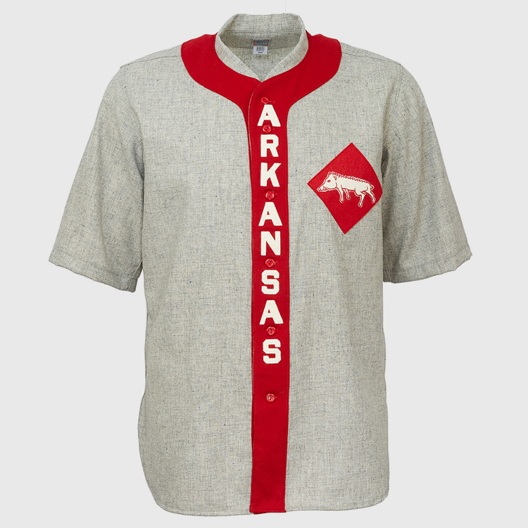 The EFF University of Arkansas 1912 Road Jersey is a gray, short-sleeve college baseball shirt with a red vertical stripe reading ARKANSAS in white and a red diamond patch featuring a white razorback logo—an authentic vintage reproduction.
