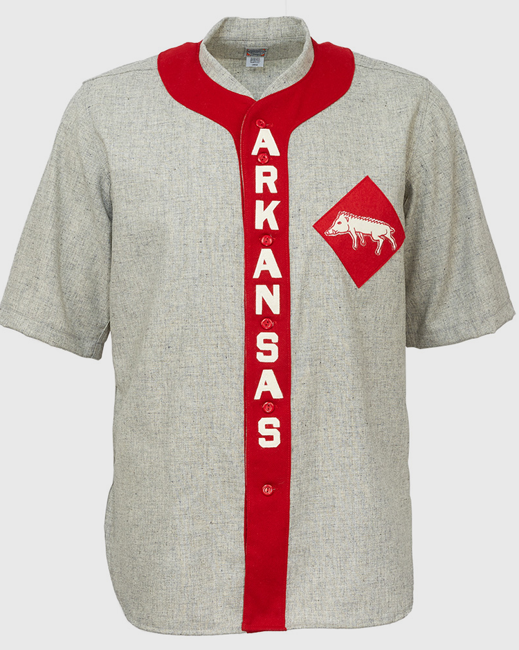 The EFF University of Arkansas 1912 Road Jersey is a gray, short-sleeve college baseball shirt with a red vertical stripe reading ARKANSAS in white and a red diamond patch featuring a white razorback logo—an authentic vintage reproduction.