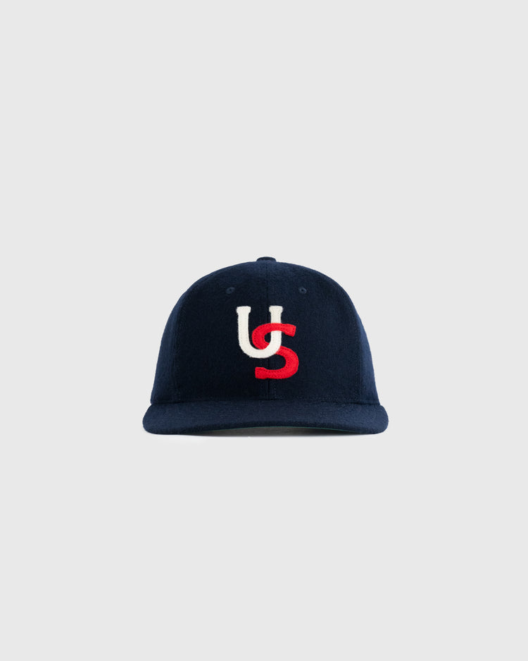 The US All-Stars 1957 Authentic Wool Ballcap by Ebbets Field Flannels features navy wool with white and red interlocking U and S embroidery, replicating the classic look of the 1957 team cap against a light gray background.