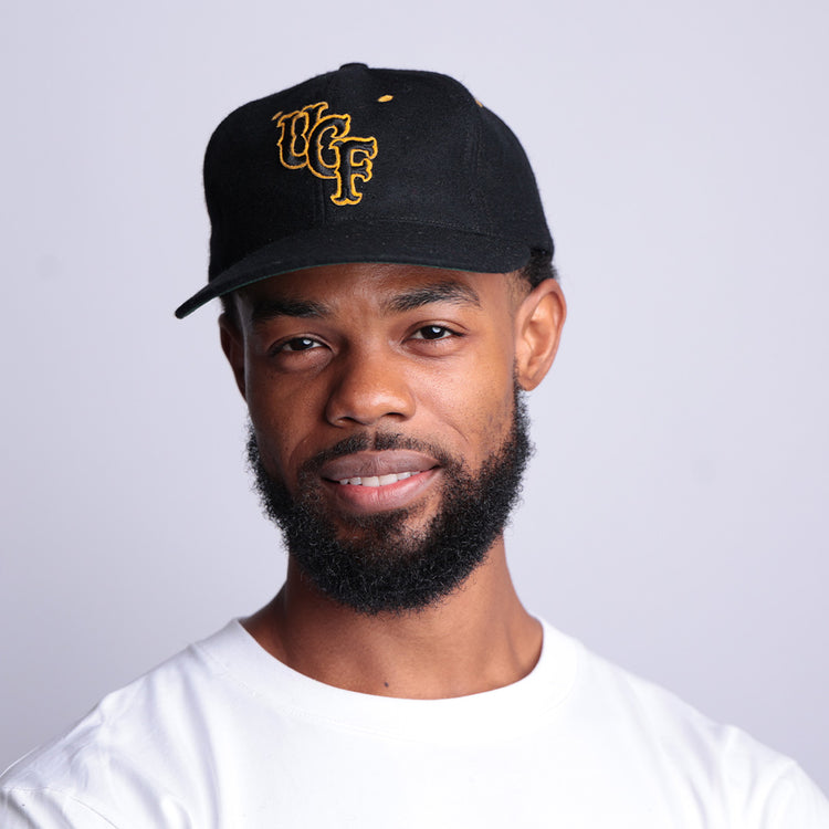 A man with a short beard and mustache wears an EFF University of Central Florida Vintage Ballcap and a white shirt, smiling slightly against a plain light gray background.