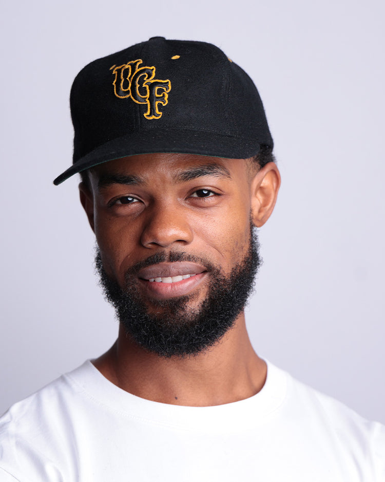 A man with a short beard and mustache wears an EFF University of Central Florida Vintage Ballcap and a white shirt, smiling slightly against a plain light gray background.