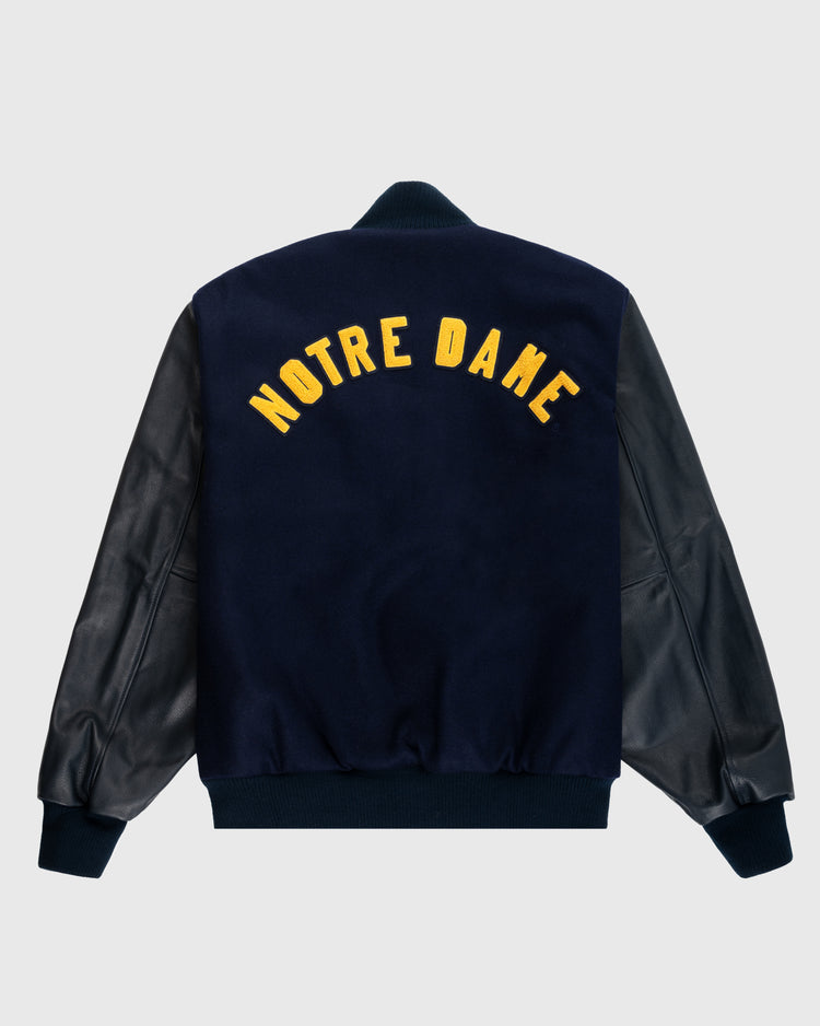 The EFF University of Notre Dame Authentic Wool & Leather Varsity Jacket has black leather sleeves, a navy wool back, and NOTRE DAME in large yellow letters across the upper back.