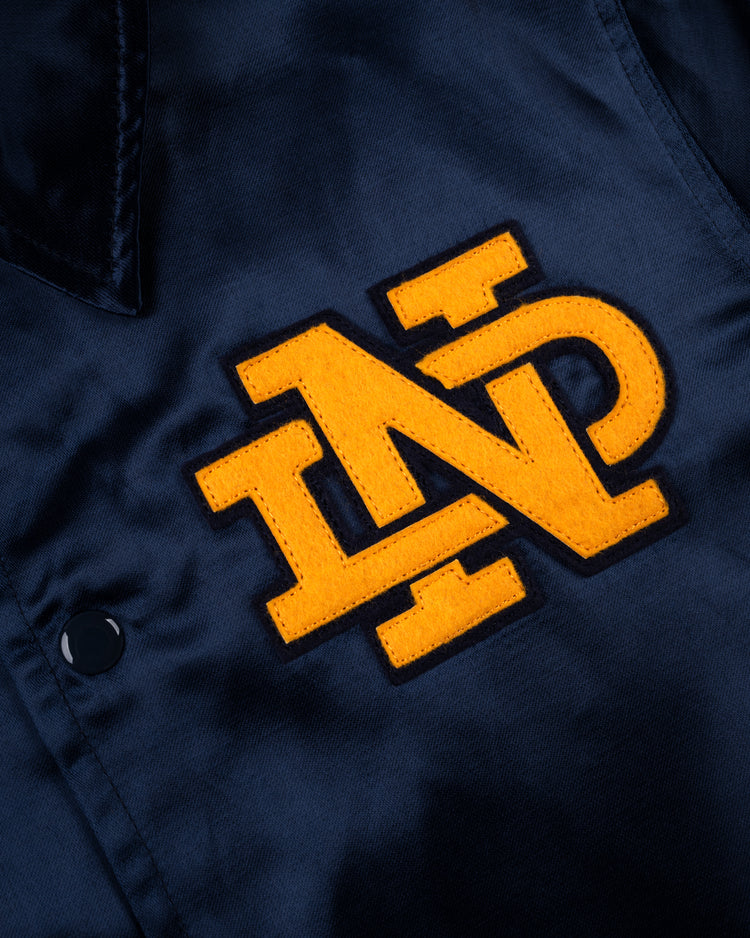A close-up of the EFF University of Notre Dame Satin Windbreaker Jacket, featuring a dark blue vintage-inspired coach’s style with a large yellow ND logo outlined in black and a black snap button on the left side.