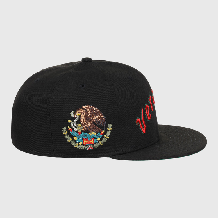 The EFF Veracruz Azules NLB Team Color Fitted Ballcap is a black hat with red cursive text on the front panel and an embroidered Mexican coat of arms on the side.