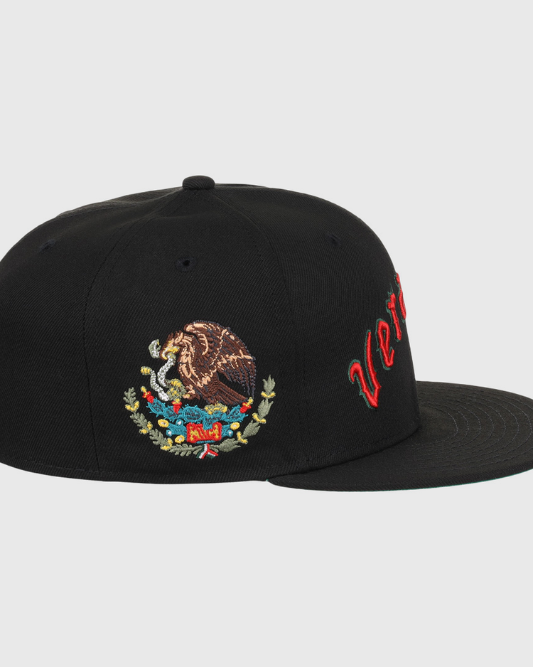 The EFF Veracruz Azules NLB Team Color Fitted Ballcap is a black hat with red cursive text on the front panel and an embroidered Mexican coat of arms on the side.