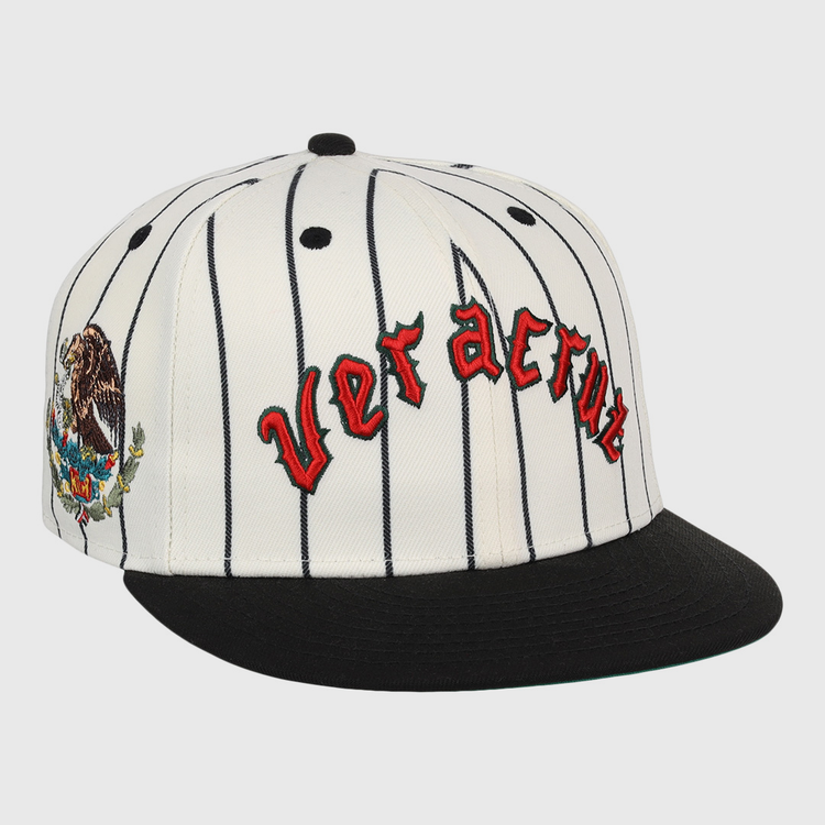 The Veracruz NLB Pinstripe Fitted Ballcap by EFF is a white cap with black pinstripes, a black brim, Veracruz in red gothic letters on the front, and an eagle-and-cactus embroidered patch on the side.
