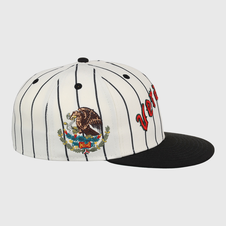 The EFF Veracruz NLB Pinstripe Fitted Ballcap features white fabric with black pinstripes, a black brim, side embroidery of the Mexican coat of arms, and partially visible red letters on the front.