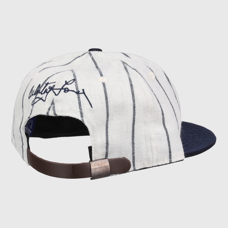 The Ebbets Field Flannels Whitey Ford Signature Series Ballcap features white fabric with dark pinstripes, a navy brim, an adjustable brown leather strap, and a black signature on the back for classic vintage style.