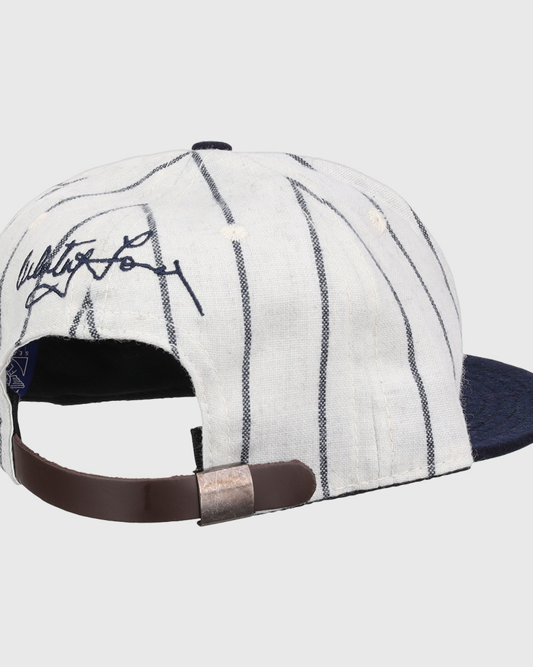 The Ebbets Field Flannels Whitey Ford Signature Series Ballcap features white fabric with dark pinstripes, a navy brim, an adjustable brown leather strap, and a black signature on the back for classic vintage style.