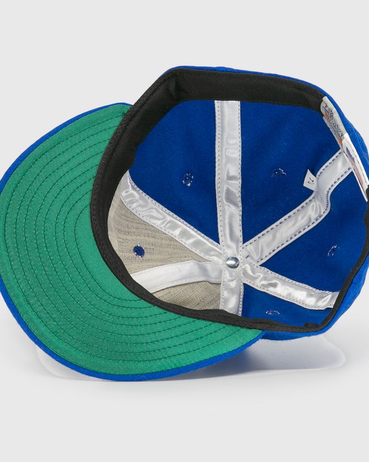 The image shows the inside of an EFF Wichita Falls Spudders 1956 Vintage Ballcap, featuring a blue wool exterior, green brim underside, silver inner seam lining, and a white tag on the inner band.