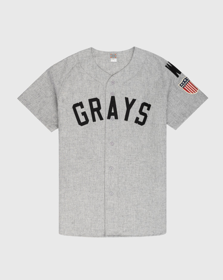 The Ebbets Field Flannels Homestead Grays 1944 Authentic Wool Road Baseball Jersey features short sleeves, GRAYS in black on the front, a U.S. flag patch on the left sleeve, and is crafted from authentic wool flannel for true vintage feel.