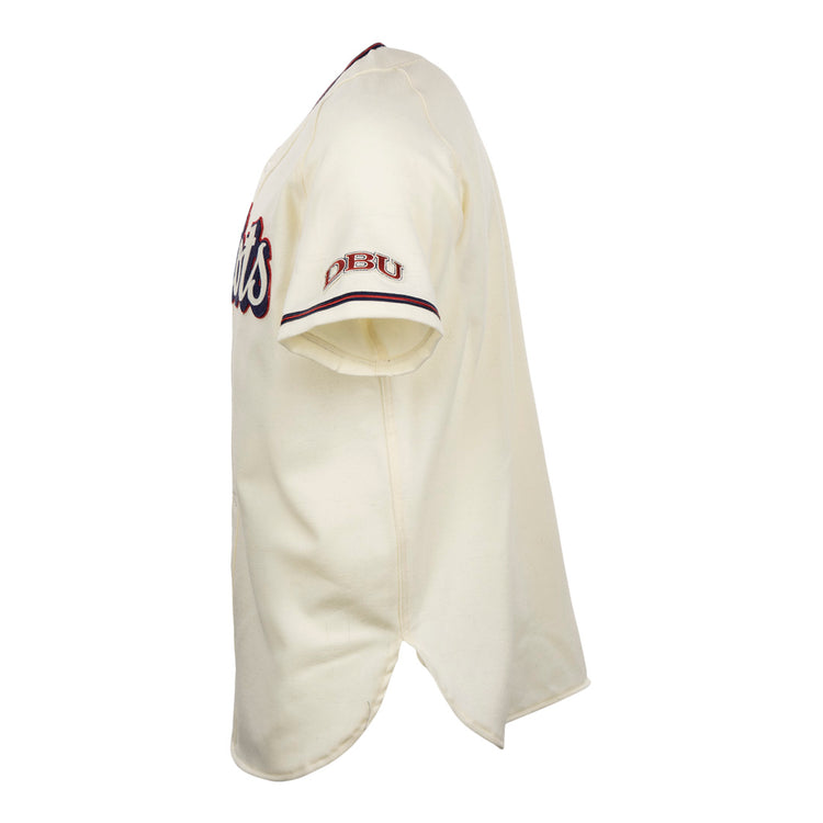 Side view of the EFF Dallas Baptist University Home Jersey: short-sleeve, cream-colored with red and blue accents. DBU is embroidered on the sleeve, a script logo appears on the chest, and it features a split bottom hem.