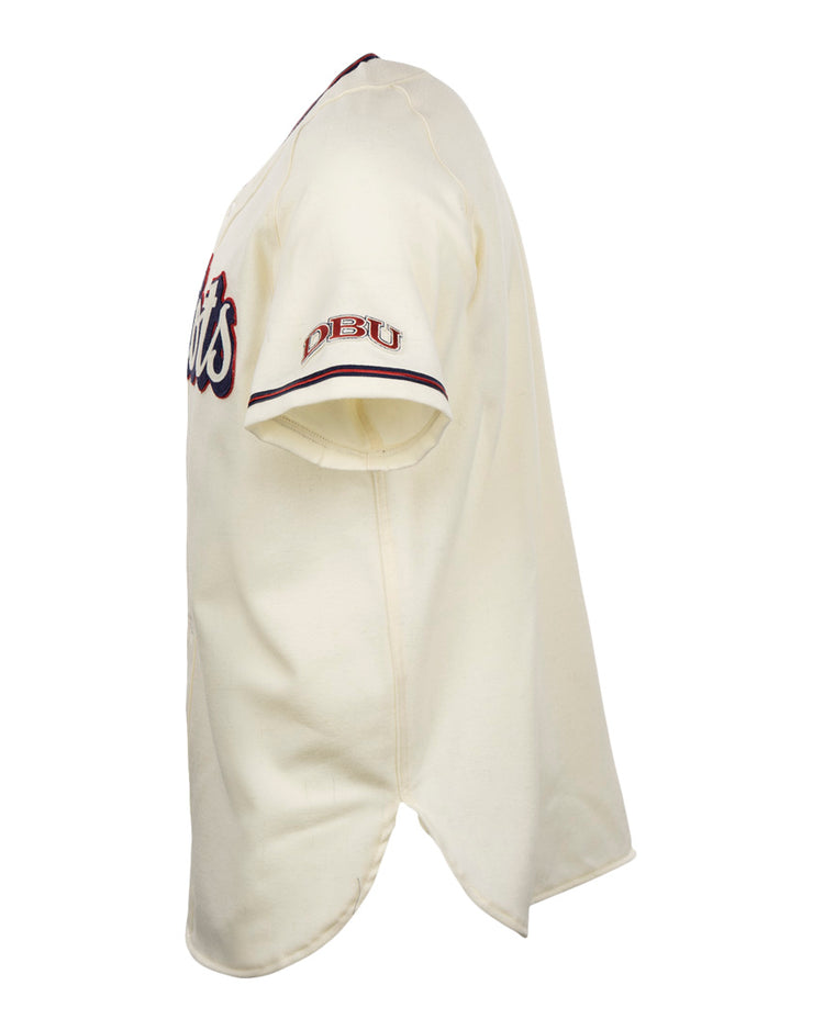 Side view of the EFF Dallas Baptist University Home Jersey: short-sleeve, cream-colored with red and blue accents. DBU is embroidered on the sleeve, a script logo appears on the chest, and it features a split bottom hem.