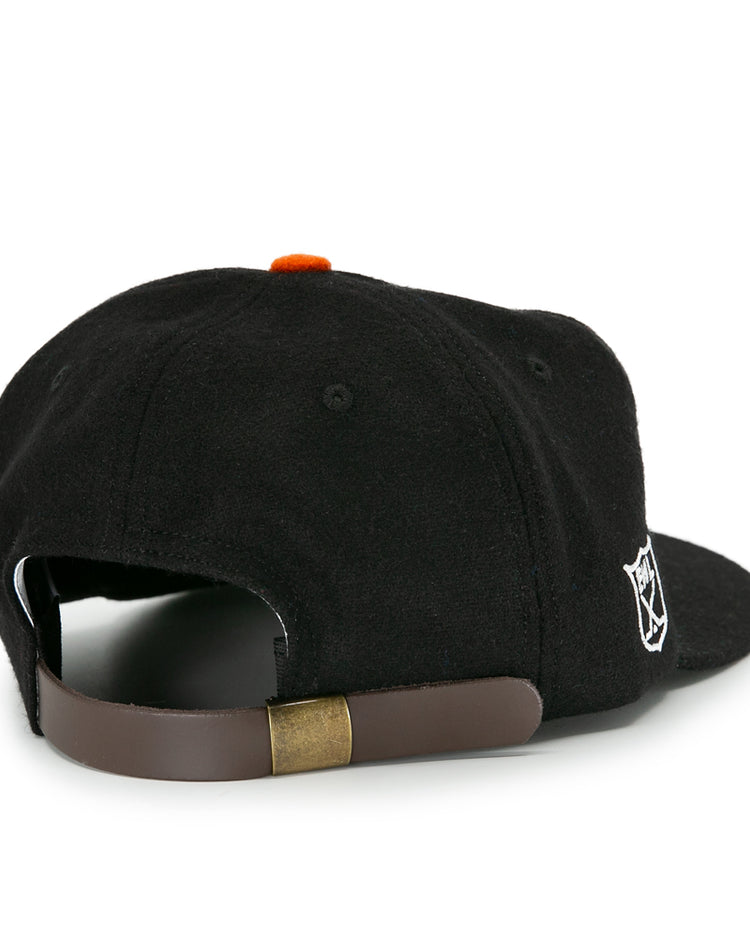 The EFF Baltimore Clippers 1962 Vintage Ballcap features black wool, a brown adjustable strap with brass buckle, and a small white embroidered logo—a timeless nod to the AHL team’s heritage.
