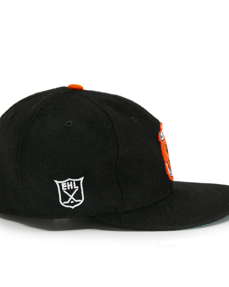The EFF Baltimore Clippers 1962 Vintage Ballcap is a black wool cap with an orange front logo and a white shield-shaped EHL emblem on the side, inspired by the original team, shown from a side angle against a white background.