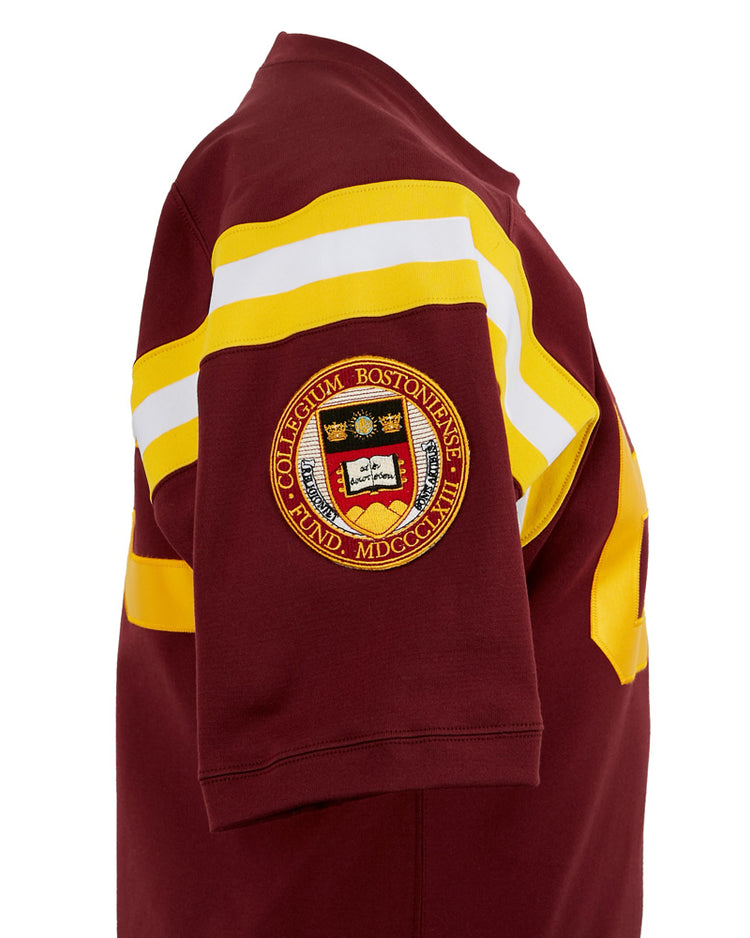 The EFF Boston College 1963 Durene Football Jersey is a maroon short-sleeve shirt with yellow and white sleeve stripes and an authentic embroidered Boston College Football Jersey patch on the upper arm.